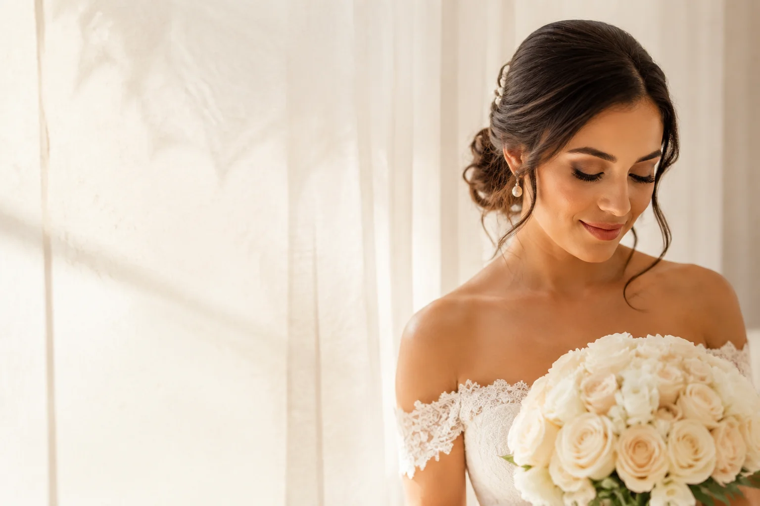 Bride with soft glam makeup and a low updo with a pearl hair pin, holding a bouquet of white roses